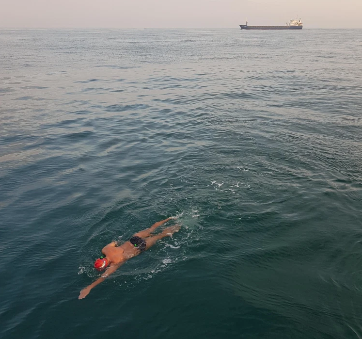 Man swimming in English Channel with shipping tanker in background